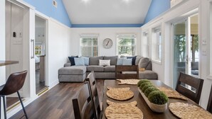 A living room with a sofa, dining table, chairs, and a clock on the wall. - Ferry Breeze Beach House – NC Coastal Escape (Minnesott Beach)