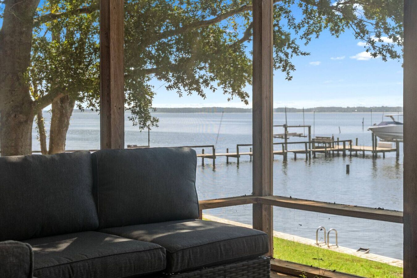 Ein Zimmer mit einer Couch, die zu einem großen Fenster mit Blick auf ein Gewässer, Stege und Boote ausgerichtet ist.