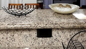Une cuisine dotée de plans de travail en granit, d’un grand saladier blanc et de luminaires suspendus.