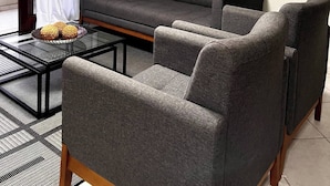 Un salon moderne avec un canapé gris, deux fauteuils, une table basse en verre et des œuvres d’art abstraites accrochées au mur.