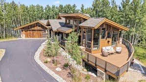 Une maison en rondins moderne, dotée d’une terrasse incurvée, de grandes fenêtres et de fondations en pierre.