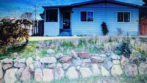 A single-story house with a front porch, a stone wall in front, and a clear sky.