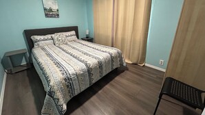 A bedroom with a bed, a nightstand, a chair, a picture on the wall, and a window with curtains.