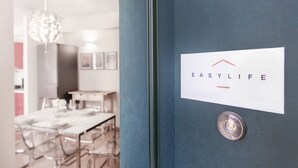 A modern kitchen with a dining area, a blue door with a sign reading "EASYLIFE," and a hanging light fixture.