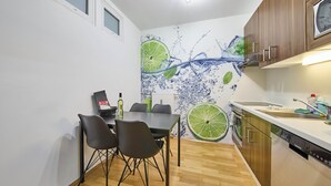 Une cuisine compacte avec un coin repas, des meubles en bois, un lave-vaisselle et une fresque murale sur le thème du citron vert.