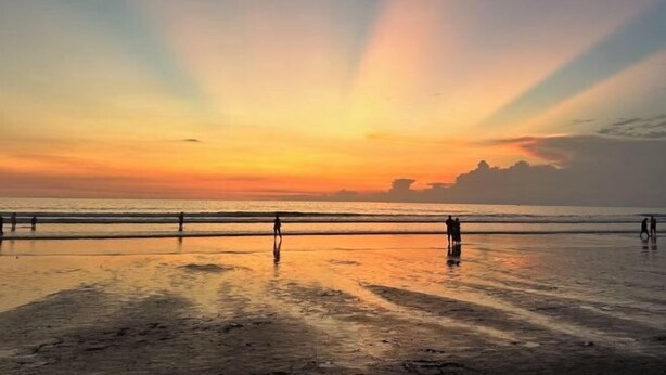 Une plage au coucher du soleil, avec des silhouettes de personnes et une rambarde.