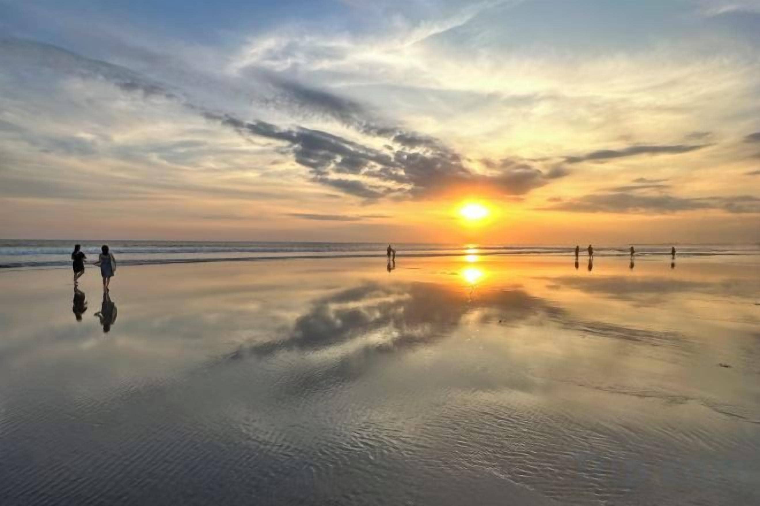 A beach scene with a sunset, calm water, and silhouettes of people.