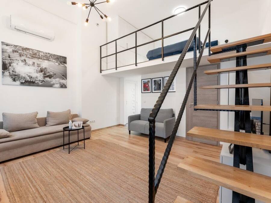 A modern loft-style living room with a high ceiling, a staircase, and a loft bed.
