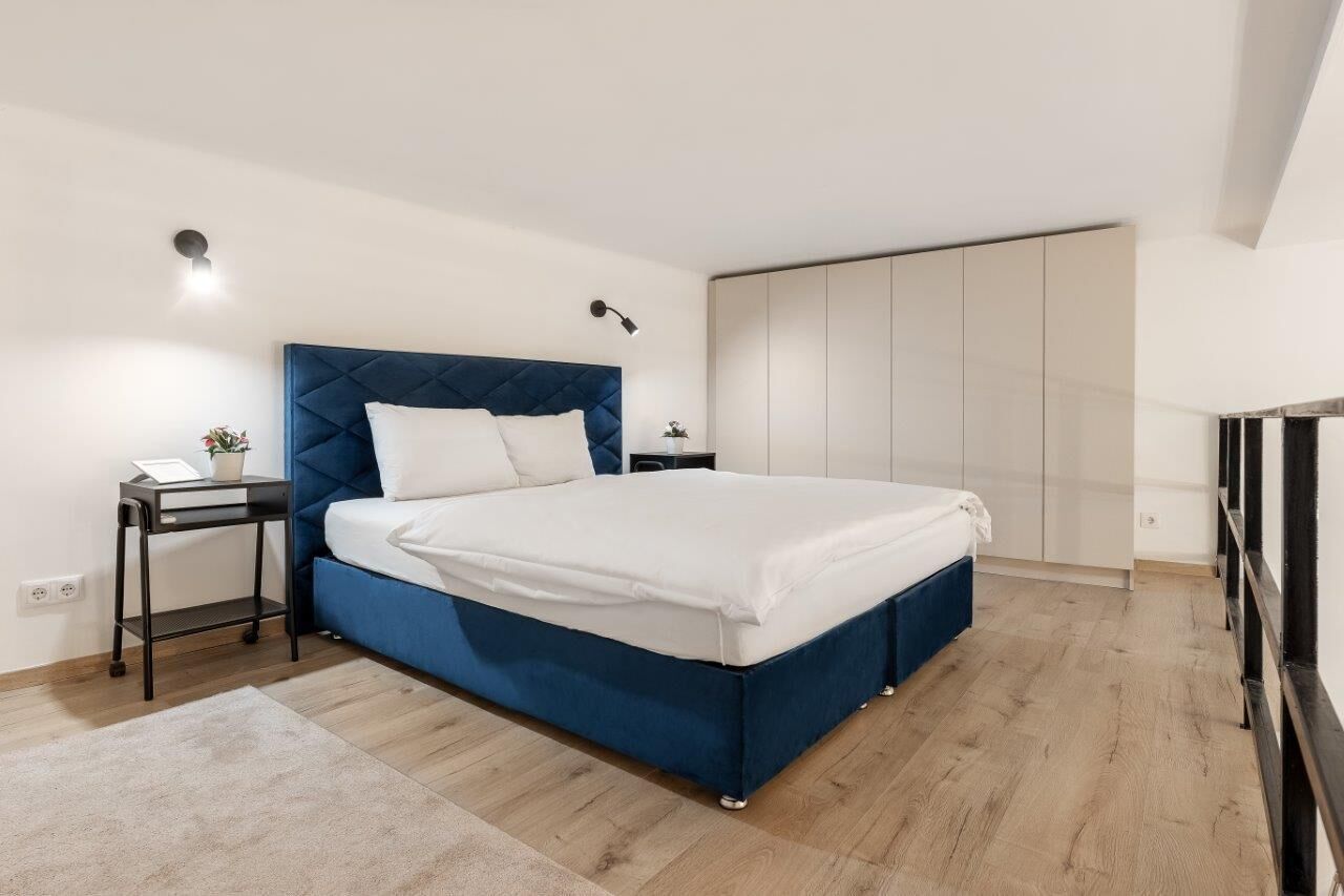 A modern bedroom with a large bed, a nightstand, a bedside table, and a wardrobe.