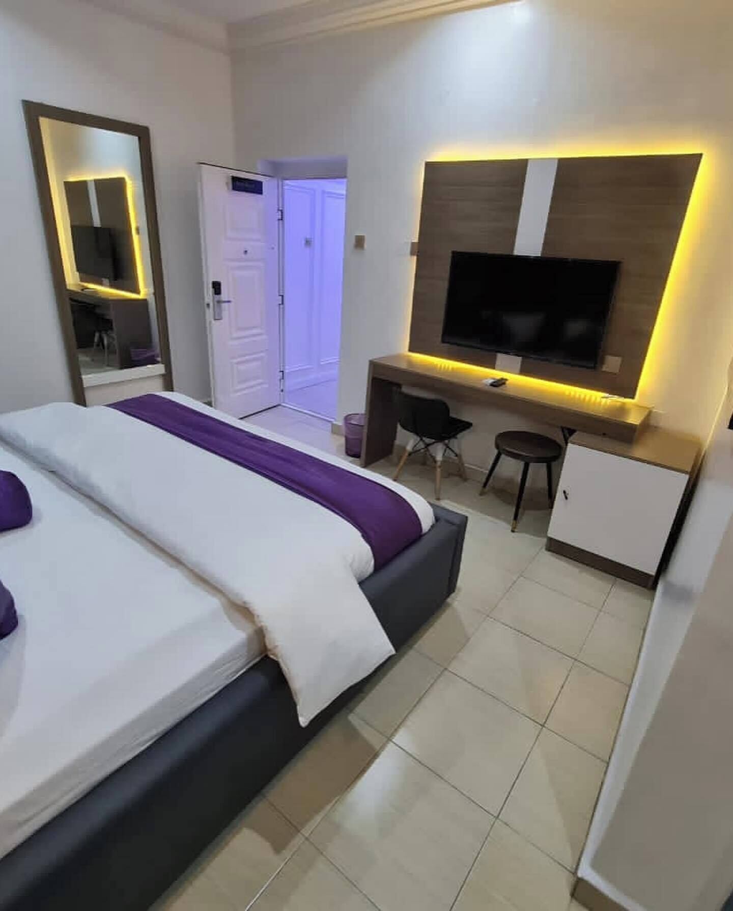 Een hotelkamer met een bed, bureau, stoel, televisie en spiegel.