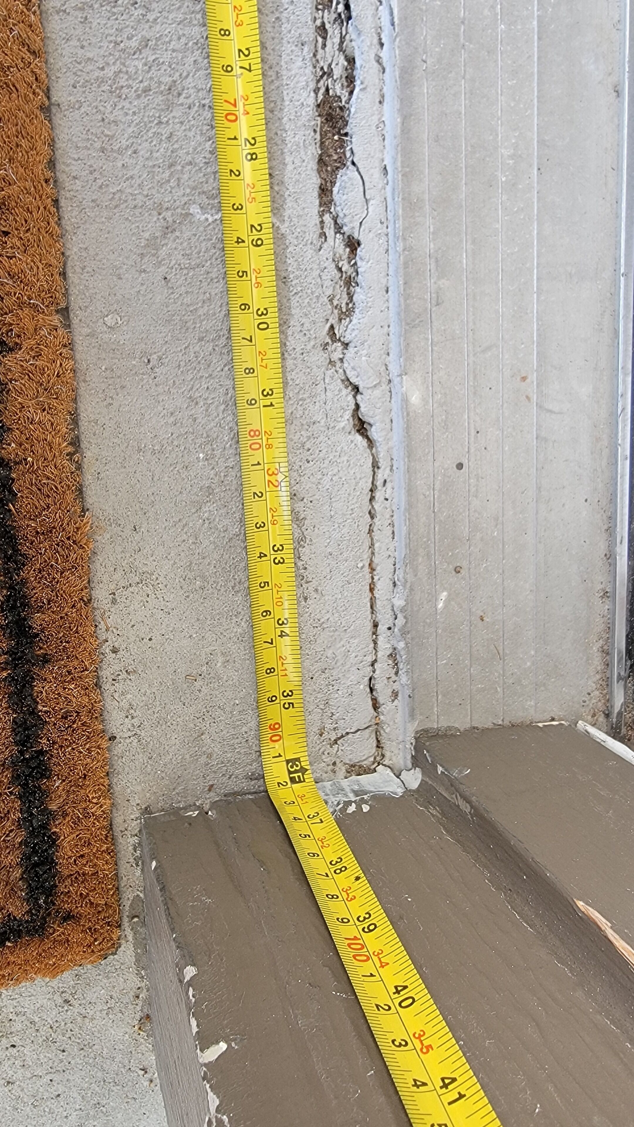 A yellow measuring tape against a wall with visible damage and a brown carpet.