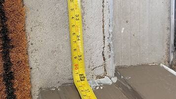 A yellow measuring tape against a wall with visible damage and a brown carpet.