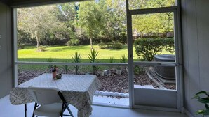Ein Zimmer mit einem großen Schiebeglasfenster, das zu einem Garten führt. Innen befindet sich ein Tisch mit Tischdecke und ein Stuhl.