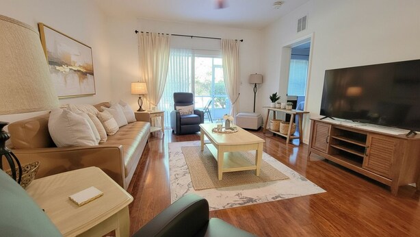 Ein Wohnzimmer mit Sofa, Sesseln, Couchtisch, TV-Schrank und Blick ins Freie.