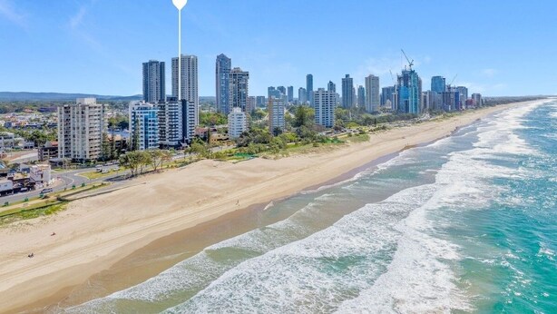 Un paysage urbain côtier avec de hauts immeubles, une plage de sable et un ciel bleu dégagé.