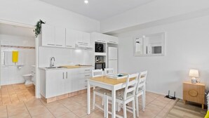 Une cuisine moderne avec des meubles blancs, une table à manger en bois et une petite table d’appoint avec une lampe.