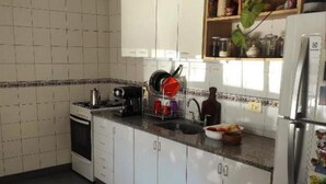 Une cuisine avec des meubles blancs, un luminaire suspendu noir et rouge, et un réfrigérateur orné d’un aimant décoratif.