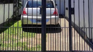 Une allée fermée par un portail mène à une maison devant laquelle est garée une voiture.