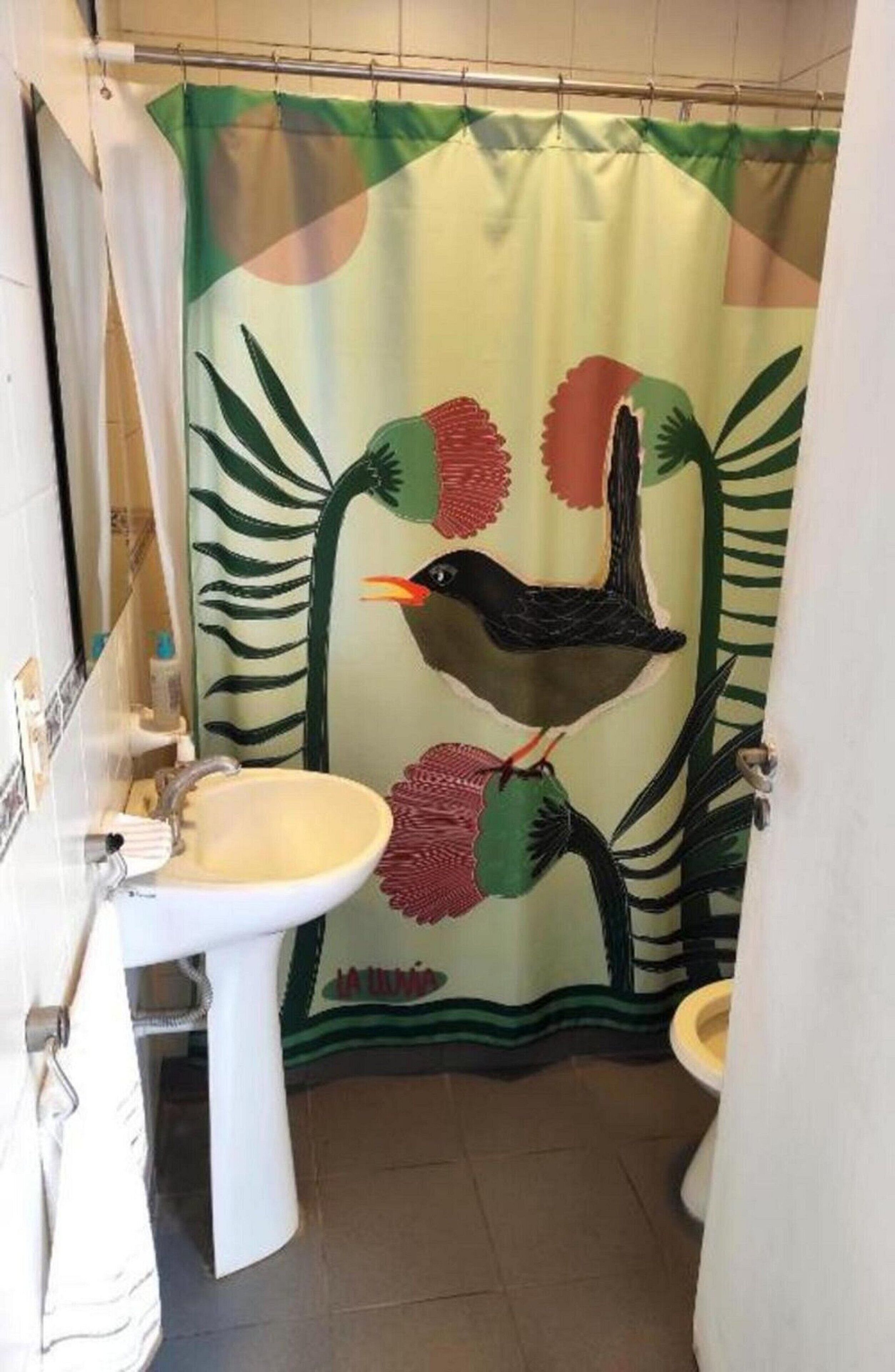 Un baño con cortina de ducha decorada con motivos de pájaros y hojas, un lavabo blanco y un inodoro.