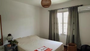 Une chambre à coucher avec un lit, une fenêtre avec des rideaux, une lampe et un plancher en bois.