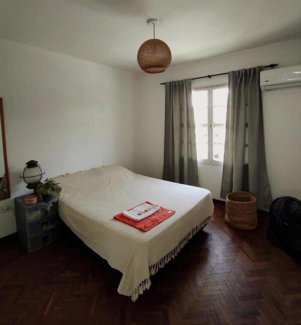 Un dormitorio con cama, ventana con cortinas, lámpara y suelo de madera.