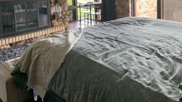 Une chambre dotée d’une cheminée en pierre, d’un grand lit et offrant une vue sur l’extérieur grâce à de grandes fenêtres.
