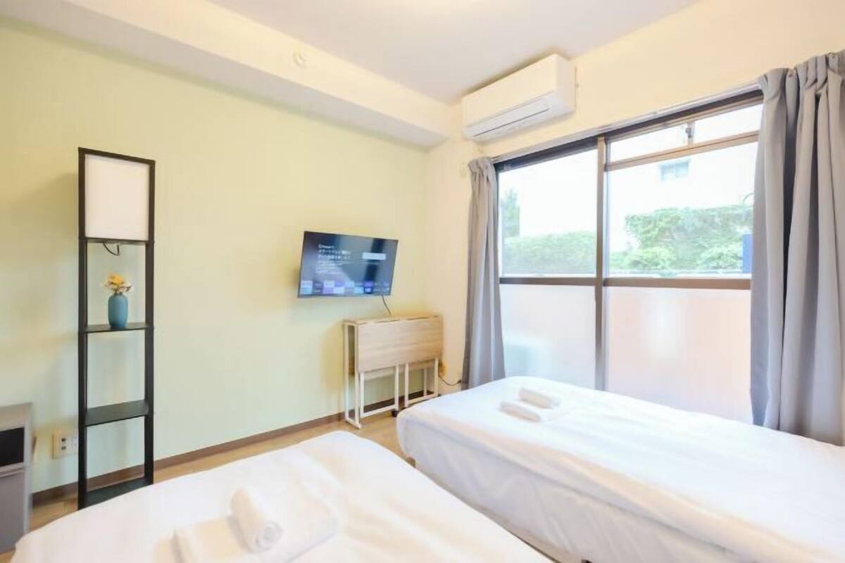 A hotel room with two beds, a TV, a desk, and a window with curtains.