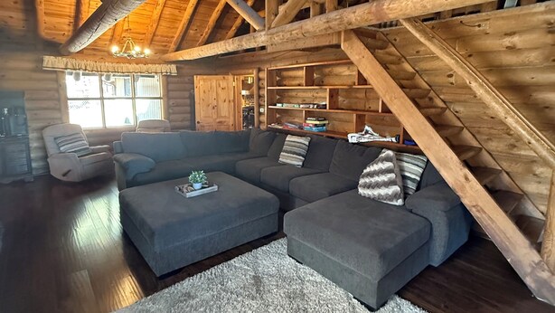 L’intérieur d’une cabane en rondins, avec un canapé d’angle, un tapis blanc et un plafond en bois.
