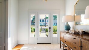 A hallway with a white door leading outside, a wooden dresser with a mirror, and a star-shaped light fixture.