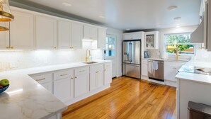 A modern kitchen with white cabinets, stainless steel appliances, and a marble countertop.