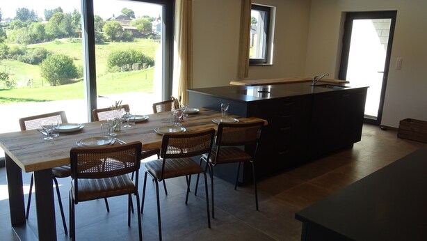 A modern kitchen with a dining area, large windows, and a view of the outdoors.