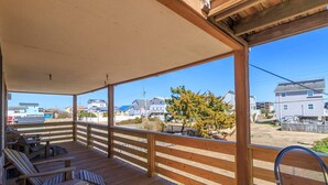 Una terraza techada al aire libre con sillas y mesa de madera, con vistas a una zona residencial con casas y un árbol.