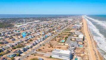 An aerial view of a coastal town with a long beach, residential areas, and a large industrial complex.