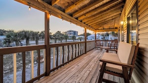 A wooden deck with a railing, a cushioned bench, and a view of palm trees and buildings.