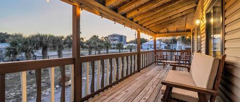 A wooden deck with a railing, a cushioned bench, and a view of palm trees and buildings.
