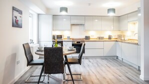 Een moderne keuken met witte kasten, een eettafel met stoelen en een ingebouwde oven.