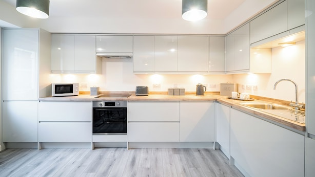 Een moderne keuken met witte kastjes, een magnetron, een broodrooster, een waterkoker en een gootsteen.