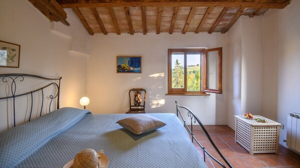 A bedroom with a bed, a window, a nightstand, and a small table with fruit.