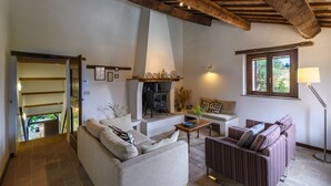 Ein gemütliches Wohnzimmer mit einer Couch, einem Sessel und einem Kamin. Ein Fenster bietet Blick auf eine grüne Umgebung.