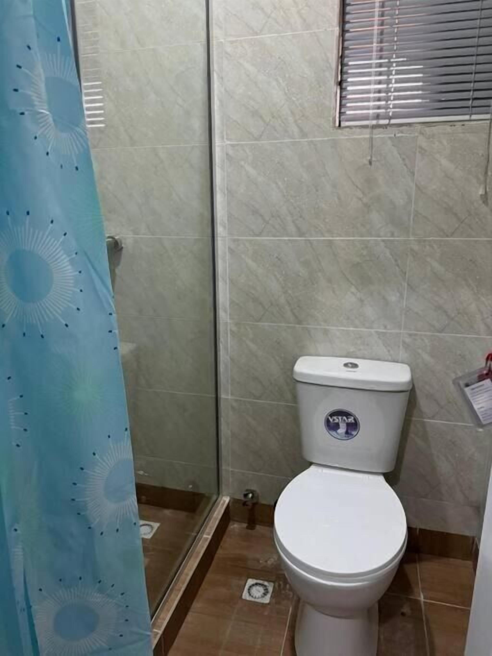 Une salle de bain avec des toilettes, un rideau de douche et des murs carrelés.