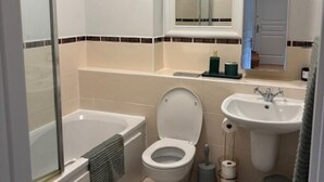 Et badeværelse med badekar, toilet, håndvask og et spejl over vasken.