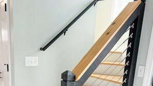 Un escalier avec des marches en bois et une rampe métallique, menant à l’étage supérieur.