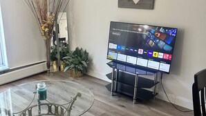Un soggiorno con un tavolino in vetro, una TV a schermo piatto e un cuore decorativo appeso al muro.