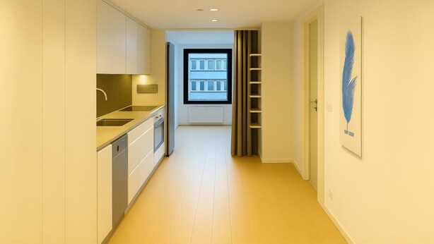 Un pasillo estrecho con una cocina a la izquierda, una ventana con persianas y una puerta a la derecha.