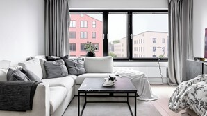 Una sala de estar moderna con un sofá, una mesa de centro y vistas a edificios a través de amplios ventanales.