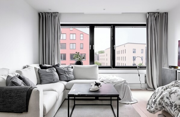Una sala de estar moderna con un sofá, una mesa de centro y vistas a edificios a través de amplios ventanales.
