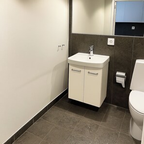 Un baño moderno con un lavamanos blanco, paredes de azulejos oscuros y un inodoro.