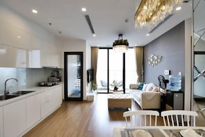 A modern hotel room with a kitchenette, a dining area, and a living space with a sofa and a table.