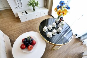 A modern living room with a round black coffee table, a white side table with fruit, and a vase with flowers.