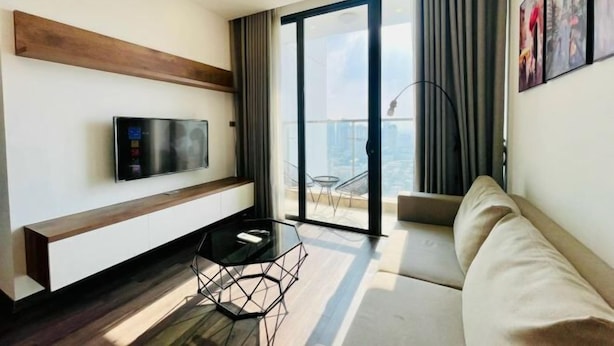 A modern living room with a flat-screen TV, a glass coffee table, a sofa, and a balcony with a view.